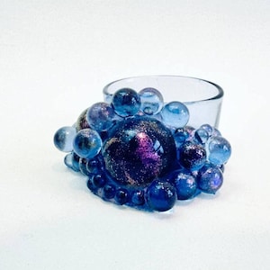 Op de afbeelding: Een glazen kaarsenhouder met een blauw en paars iriserend bubbelontwerp.
