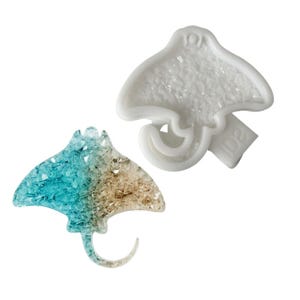 May include: A stingray-shaped silicone mold in white and a finished stingray-shaped resin charm featuring a gradient of translucent turquoise and tan colors with a textured, glittery appearance. The mold has the text ID2 embossed on its side.