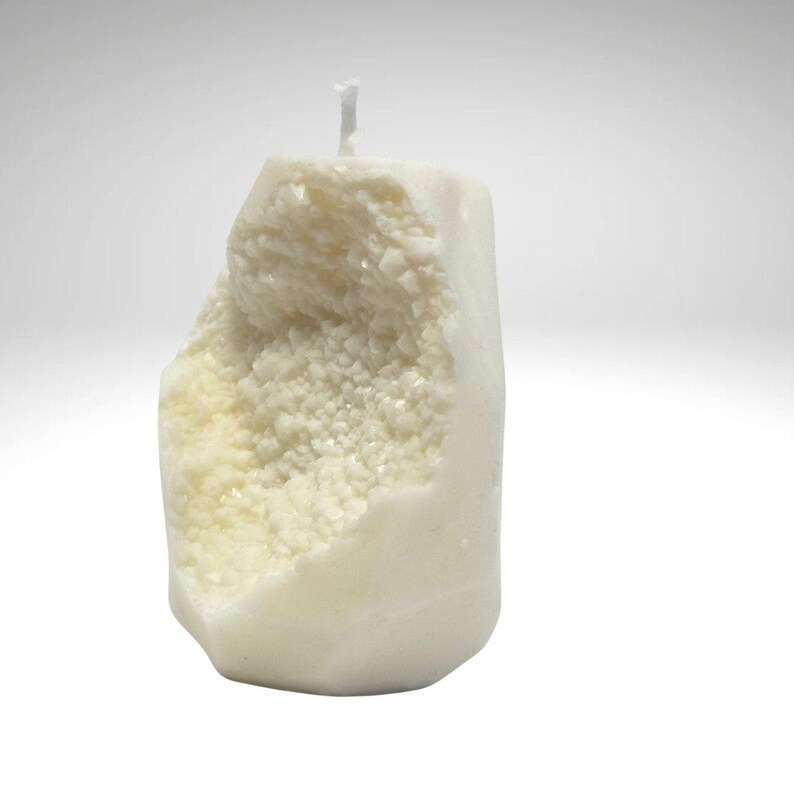 Op de afbeelding: Een witte kaars in de vorm van een rots met een ruw, getextureerd oppervlak. De kaars heeft een witte lont en is gemaakt van natuurlijke was.