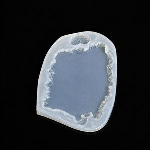 Peut inclure: Un pendentif bleu clair de forme irrégulière avec une bordure blanche texturée. Le pendentif a un trou en haut et un intérieur lisse bleu clair. Le fond est noir.