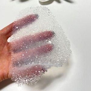 Könnte beinhalten: Eine transparente, durchsichtige Folie aus Luftpolsterfolie, die in einer Hand gehalten wird. Die Luftpolster sind klein und gleichmäßig groß und erzeugen eine strukturierte Oberfläche.