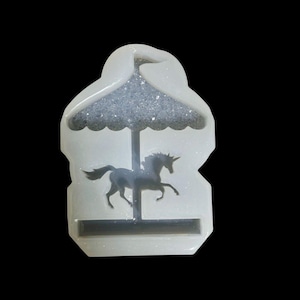 May include: A clear resin carousel-shaped mould. It features a unicorn silhouette and a glittery, silver top. This mould is designed for crafting and creating decorative items.