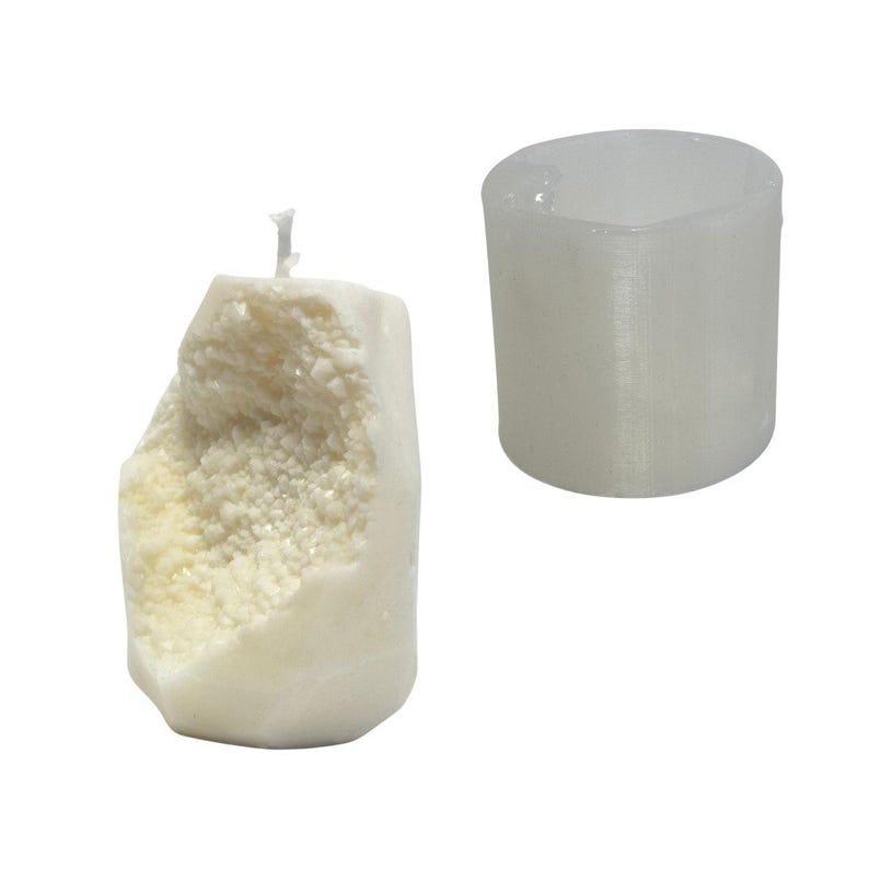 Op de afbeelding: Een witte kaars met een ruw, getextureerd oppervlak, dat lijkt op een rotsformatie. De kaars ligt naast een doorzichtige plastic mal.
