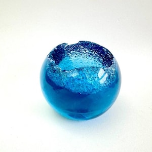 Peut inclure: Un petit bol rond en verre bleu avec un bord blanc rugueux. Le bol est rempli d'un liquide bleu clair.