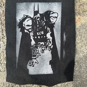 May include: A black and white graphic print of Batman, with the word "ICE" on the chest, on a black fabric. The image is rectangular and features a stylized depiction of the superhero, with his iconic bat symbol.