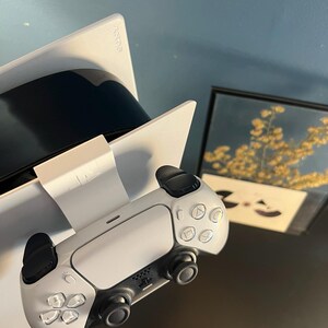 May include: A white and black PlayStation 5 console with a matching controller. The controller has a symmetrical design with black thumbsticks and buttons. The console is angled, showing the Sony logo.