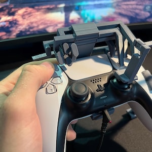May include: A gray 3D-printed controller attachment is mounted on a black and white game controller. The attachment has a series of levers and buttons. The screen in the background displays the text "Touch your Bloodstain".
