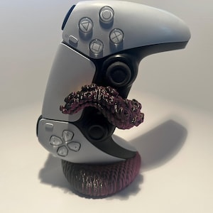 May include: A white and black gaming controller with a purple and brown decorative accent. The controller has multiple buttons and a textured base. The accent appears to be a stylized organic shape.