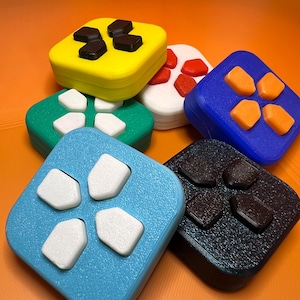 May include: A collection of colorful, square-shaped game controller buttons. The buttons are in various colors, including yellow, green, blue, white, and black, each with contrasting button shapes. The image is set against an orange background.