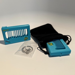 May include: A light blue miniature keyboard toy with a black drawstring bag and a small bag of silver keychains. The keyboard has vertical white lines and a small green bear graphic. The items are on a white surface.