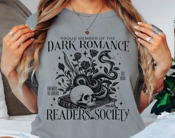 May include: A grey t-shirt featuring a black graphic print of a skull resting on a book, surrounded by roses and a coiled snake. The text reads: PROUD MEMBER OF THE DARK ROMANCE READERS SOCIETY, ENEMIES TO LOVERS, and EST 1890.