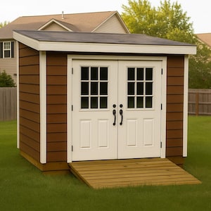 May include: A brown wooden shed with a black roof and white-framed double doors. The doors have multiple glass panes and black handles. A wooden ramp leads to the entrance, set on a green lawn.