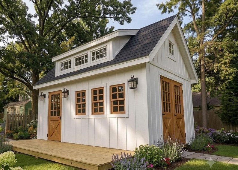 May include: A white shed with vertical siding, a dark shingled roof, and natural wood doors and window frames. The structure features a front wooden deck, multiple windows, and black exterior wall-mounted lanterns on the white facade.