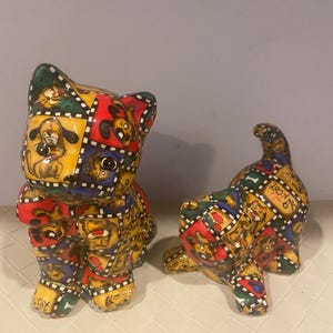 May include: Two ceramic dog figurines. One is upright, the other is in a playful pose. Both are decorated with a colorful pattern of cartoon dogs, red, yellow, green, and blue. The figurines have a glossy finish.