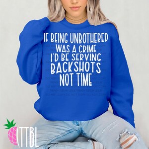 May include: Royal blue sweatshirt with the text "IF BEING UNBOTHERED WAS A CRIME I'D BE SERVING BACKSHOTS NOT TIME" in white. The sweatshirt is worn by a person wearing blue jeans.