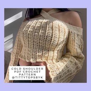 Op de afbeelding: Een gehaakt top met open schouders en een gekruiste halternek. De top is lichtbeige van kleur en heeft een losse, vloeiende pasvorm. De tekst "COLD SHOULDER PDF CROCHET PATTERN @TITTYTOPSBYK" is zichtbaar onderaan de afbeelding.