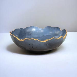 May include: A large, gray ceramic bowl with a gold rim. The bowl has an irregular, wavy edge.