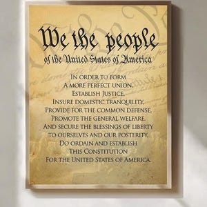 May include: A rectangular wall art print featuring the Preamble to the United States Constitution. The text is printed in black on a tan, parchment-style background with a faint, faded historical document overlay and a light-coloured frame border.