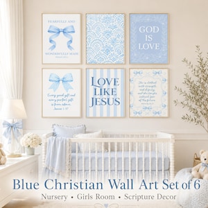 May include: A set of six framed blue Christian wall art prints. The prints feature bows, floral patterns, and inspirational quotes like "God is Love" and "Love Like Jesus." The nursery decor is designed for a girl's room.