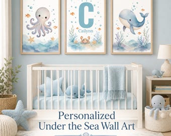 May include: A set of three framed wall art prints featuring watercolor illustrations of an octopus, a crab with the letter C and the name Cailynn, and a whale, all surrounded by bubbles, seaweed, and small fish in shades of blue and orange.