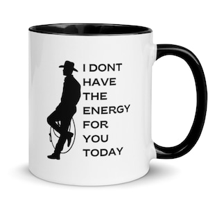 May include: White coffee mug with a black rim and handle. The mug has a black silhouette of a cowboy with the text "I don't have the energy for you today".