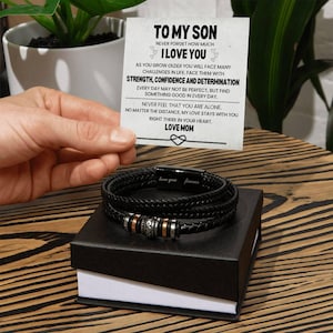 Peut inclure: Un bracelet en cuir noir avec un fermoir argenté et un petit charme argenté. Le bracelet est dans une boîte noire avec une carte blanche qui dit "To My Son Never Forget How Much I Love You" et un message sur la force, la confiance et la détermination. La carte est signée "Love Mom".
