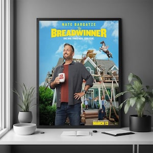 Op de afbeelding: Een ingelijste filmposter voor "The Breadwinner" met Nate Bargatze. De poster heeft een blauwe luchtachtergrond met een huis in aanbouw. Bargatze houdt een mok vast met "#2 Parent". De filmtitel is geel.