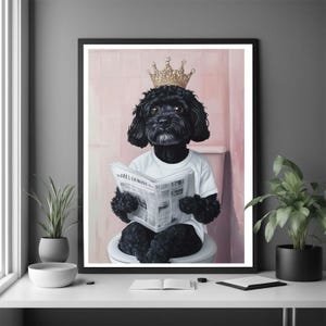 Peut inclure: Une impression d'art encadrée montre un chien noir portant une couronne dorée et un t-shirt blanc, assis sur des toilettes et lisant un journal. Le fond est rose et l'impression est affichée sur une surface blanche.