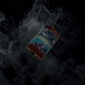 May include: A cylindrical bead featuring a central band of translucent light blue material flanked by two sections of dark brown wood with a swirling, marbled pattern of black and white resin accents integrated into the wood grain structure.