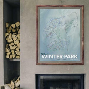 Może przedstawiać: Oprawiona mapa Winter Park, Kolorado, z jasnoniebieskim tłem i szczegółowym obrysem tras narciarskich w kolorze niebieskim, zielonym i czerwonym. Mapa jest w brązowej drewnianej ramie, z białym napisem "Winter Park".