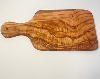 Peut inclure: Une grande planche à découper rectangulaire en bois d'olivier avec une poignée. La planche a une finition en bois naturel et un beau motif de grain.