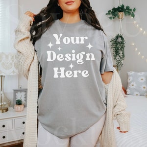May include: A gray oversized t-shirt with the text "Your Design Here" in white. The shirt is being worn by a person with long dark hair. The person is wearing white shorts and a cream cardigan.