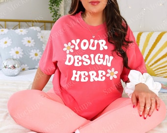 May include: A pink oversized t-shirt with short sleeves and a crew neck. The shirt has a white graphic with the text "YOUR DESIGN HERE" and two white daisies.