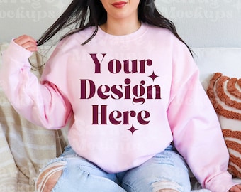 May include: A pink sweatshirt with the text "Your Design Here" in maroon lettering. The sweatshirt is being worn by a person sitting on a couch.