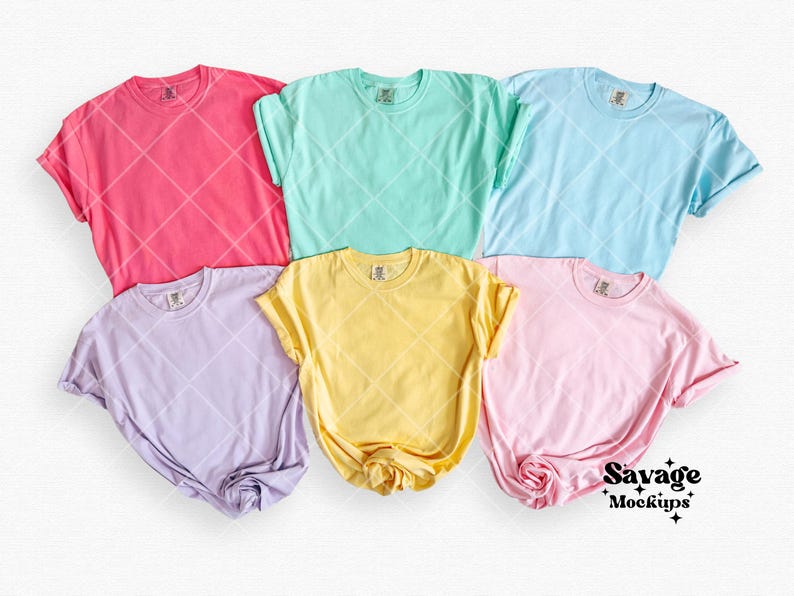 Puede incluir: Cinco camisetas en blanco de diferentes colores pastel: rosa, azul claro, amarillo, lavanda y verde menta. Las camisetas est&aacute;n dispuestas en plano sobre una superficie blanca.