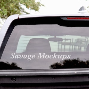 May include: A gray pickup truck with a rear window that has a white vinyl decal that says "Savage Mockups".