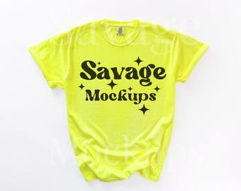 Op de afbeelding: Een felgeel T-shirt met de tekst "Savage Mockups" in zwarte letters met een retro-lettertype en ster-accenten.
