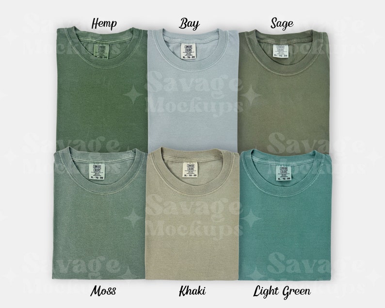 May include: Six folded t-shirts in different shades of green, including hemp, bay, sage, moss, khaki, and light green. Each shirt has a small tag with the words "Comfy Colors" on it.