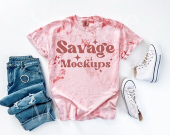 Könnte beinhalten: Ein pinkfarbenes Batik-T-Shirt mit dem Text "Savage Mockups" in brauner Schrift. Das Shirt liegt flach auf einer weißen Oberfläche mit einem Paar weißen High-Top-Sneakern und einer blauen Jeans.