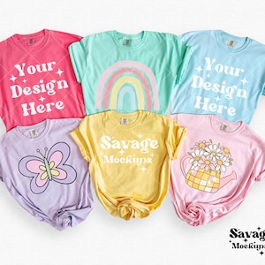 Flat lay shirt mockup showing 6 shirts in the colors Crunchberry, Island Reef, Chambray, Orchid, Butter, and Blossom. The shirts have rolled sleeves and have a white simple background.