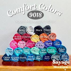 May include: A variety of youth midweight t-shirt colors rolled up and stacked in a pyramid shape. The colors include: gray, white, black, pepper, water melon, crimson, butter, melon, terra cotta, neon pink, blossom, crunch berry, orchid, violet, flo blue, topaz blue, cham ray, lagoon blue, chalky mint, island reef, sea foam, island green, china blue, washed denim, royal caribbean, ice blue, true navy, granite, and blue jean.