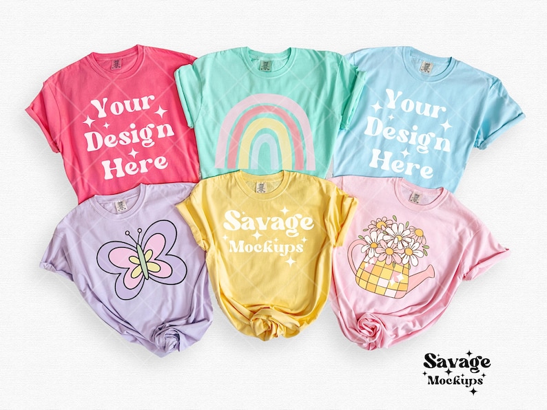 May include: Five different colored t-shirts with various designs. The shirts are laid out on a white surface. The designs include a rainbow, a butterfly, a watering can with flowers, and the text "Your Design Here" and "Savage Mockups".