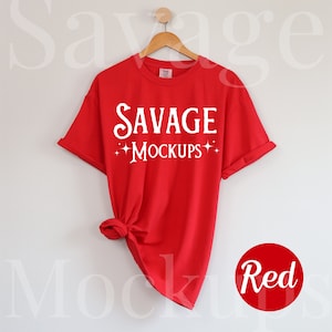 May include: Red t-shirt with the text "SAVAGE MOCKUPS" in white on the front. The shirt is hanging on a wooden hanger against a white wall.
