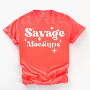 May include: A coral colored t-shirt with the text "Savage Mockups" in white. The text is in a retro font with stars around it.