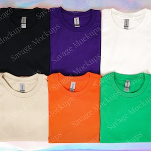 K&ouml;nnte beinhalten: Sechs gefaltete T-Shirts in verschiedenen Farben: Schwarz, Lila, Wei&szlig;, Beige, Orange und Gr&uuml;n. Jedes Shirt hat einen Rundhalsausschnitt und kurze &Auml;rmel.