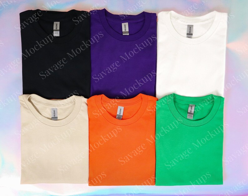 K&ouml;nnte beinhalten: Sechs gefaltete T-Shirts in verschiedenen Farben: Schwarz, Lila, Wei&szlig;, Beige, Orange und Gr&uuml;n. Jedes Shirt hat einen Rundhalsausschnitt und kurze &Auml;rmel.