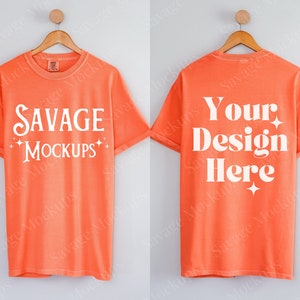 May include: Orange t-shirts displayed on a wooden hanger. The front of the shirt has the text "SAVAGE MOCKUPS" in white. The back of the shirt has the text "Your Design Here" in white. The shirts are a solid orange color.