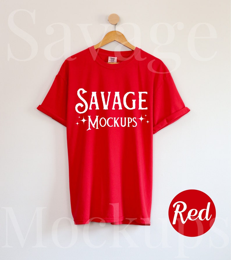 May include: Red t-shirt with the text "SAVAGE MOCKUPS" in white on the front. The shirt is hanging on a wooden hanger against a white wall.