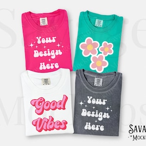 May include: Four folded t-shirts with different designs. The first shirt is pink with the text "Your Design Here". The second shirt is teal with three pink flowers. The third shirt is white with the text "Good Vibes" in pink. The fourth shirt is gray with the text "Your Design Here".