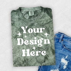 May include: A green tie-dye t-shirt with the text "Your Design Here" in white. The shirt is folded and laid on a white surface with a pair of blue jeans.